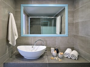 A bathroom with a white sink, a mirror, and a towel rack. - Colors In Naousa (Paros)