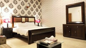 A hotel room with a bed, bedside tables, a glass coffee table, a mirror, and patterned wallpaper.