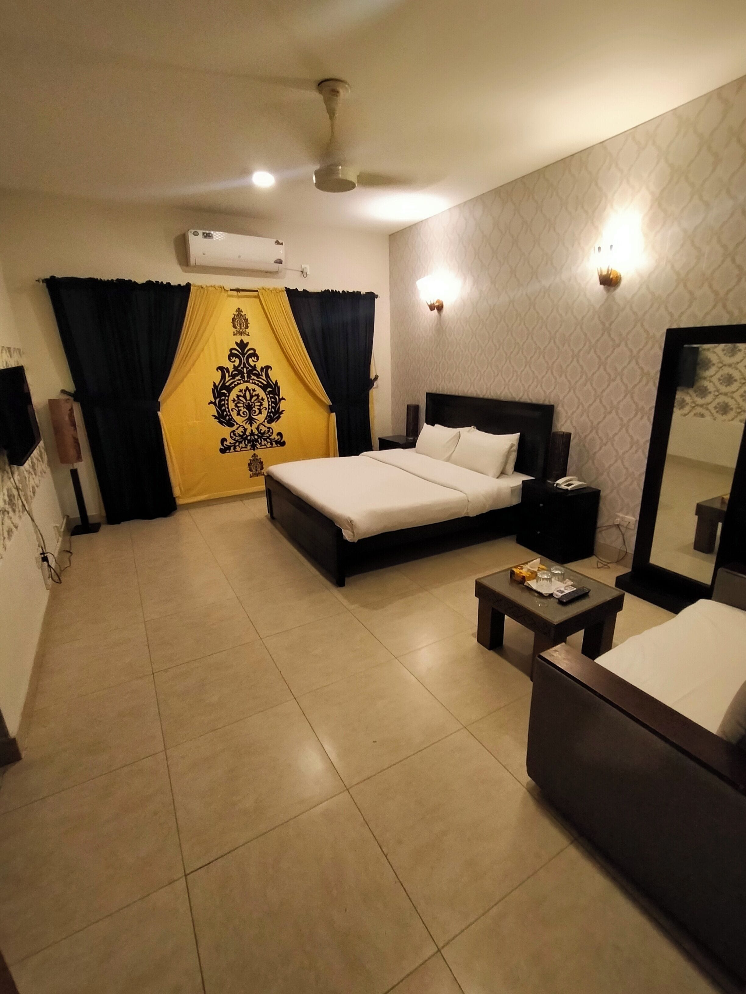 A hotel room with a bed, a bedside table, a chair, a ceiling fan, and a wall-mounted air conditioner.