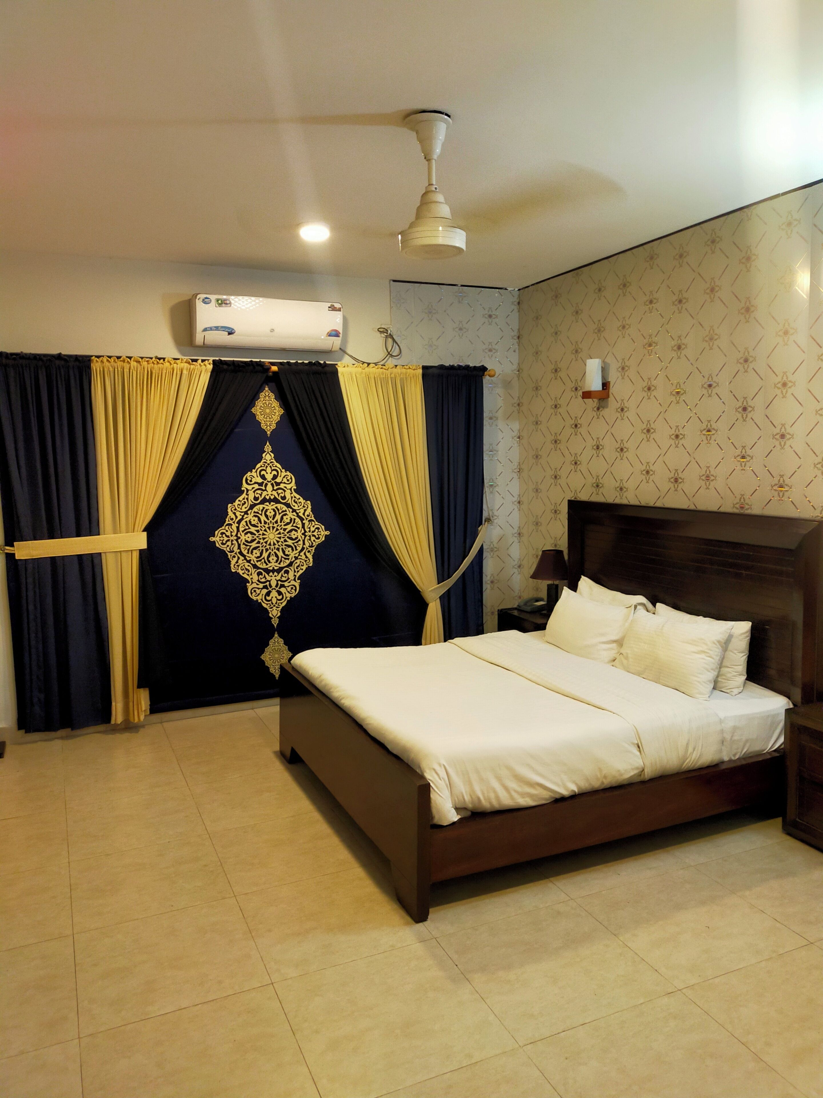 Un dormitorio con cama, cortinas, ventilador de techo, aire acondicionado y pared con diseño.