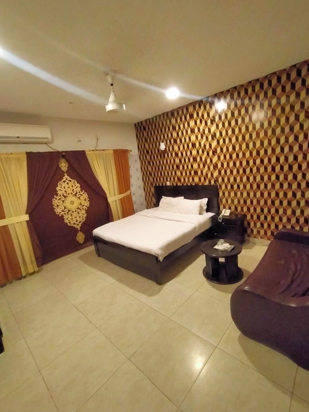 A hotel room with a bed, a small round table, a sofa, and a patterned wall.