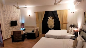 A hotel room with two beds, a desk, a chair, a television, and a ceiling fan.