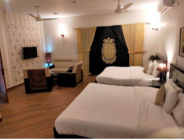 A hotel room with two beds, a desk, a chair, a television, and a ceiling fan.