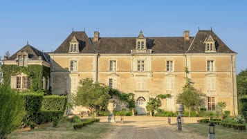 A large, historic building with multiple windows and a symmetrical facade, surrounded by a well-maintained garden with gravel paths.