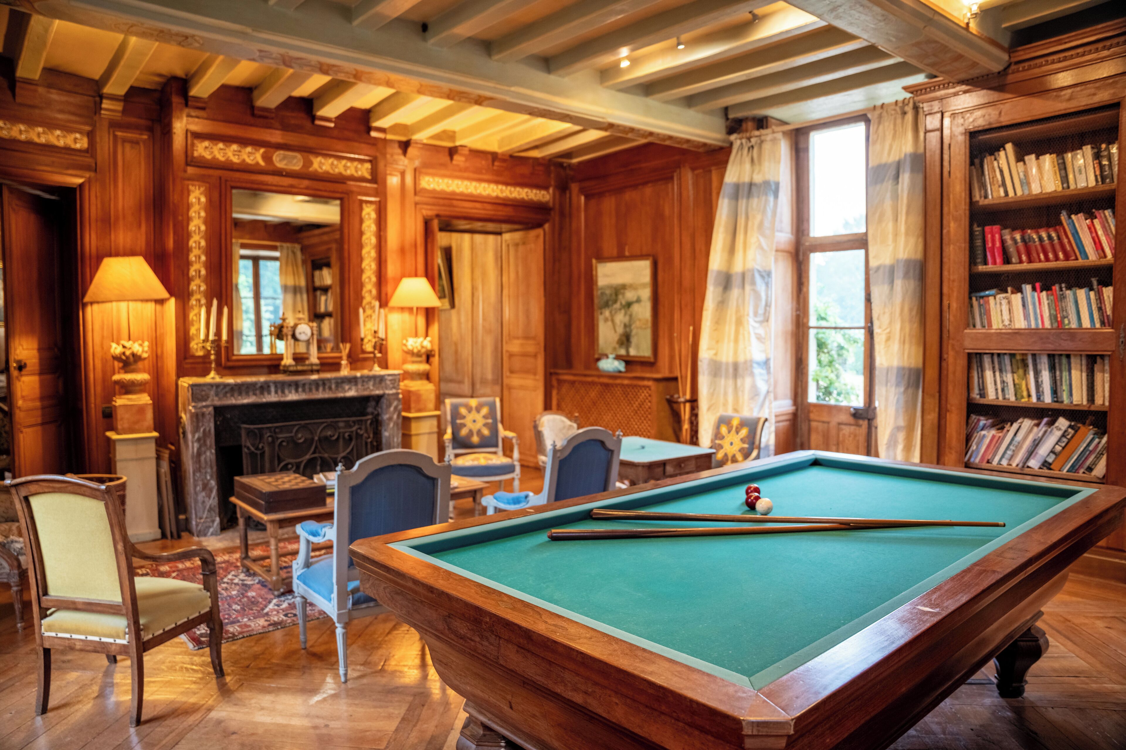 A room with a pool table, chairs, a fireplace, and a bookshelf.