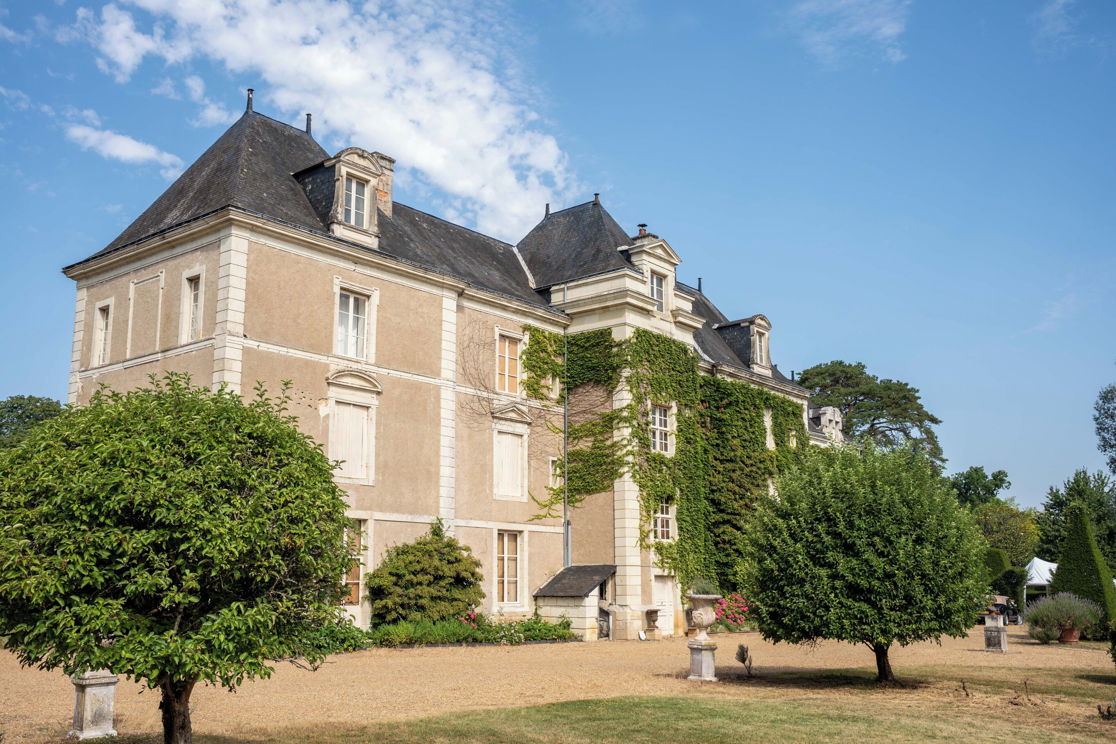 A large, historic building with a symmetrical facade, multiple chimneys, and a well-maintained garden with mature trees.