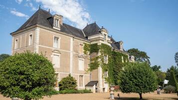 A large, historic building with a symmetrical facade, multiple chimneys, and a well-maintained garden with mature trees.