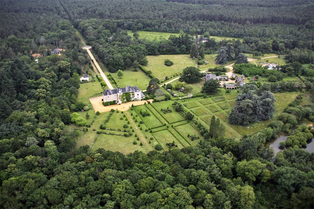 An aerial view of a large estate with multiple buildings, extensive gardens, and a river.