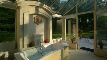 A spa area with a large bathtub, a shower, and a glass-enclosed patio with a view of the garden.