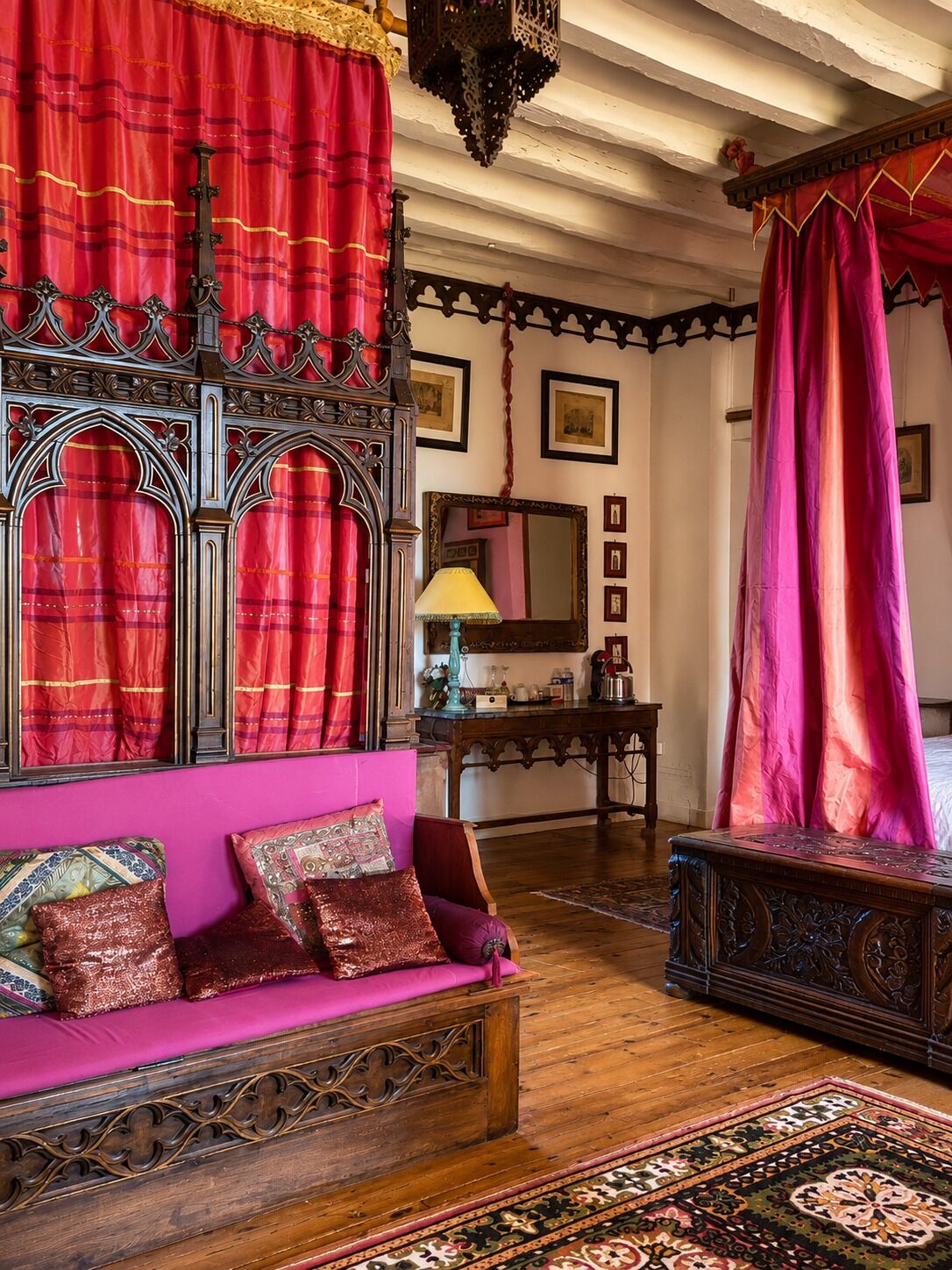 Een klassieke kamer met een houten bank, een tafel en een bed met rode gordijnen.