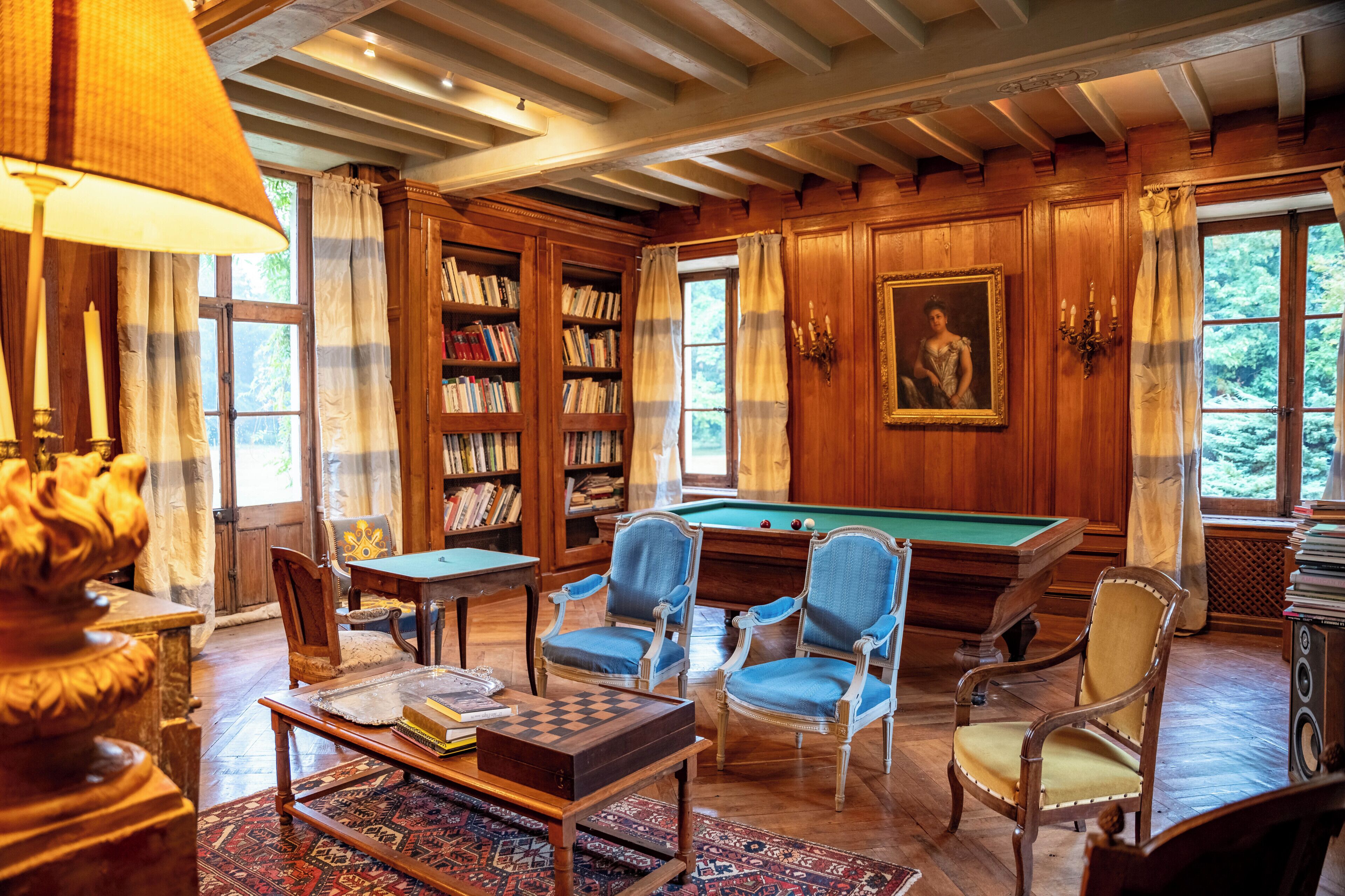 Une pièce équipée d’une table de billard, de bibliothèques et d’un porte-queue.