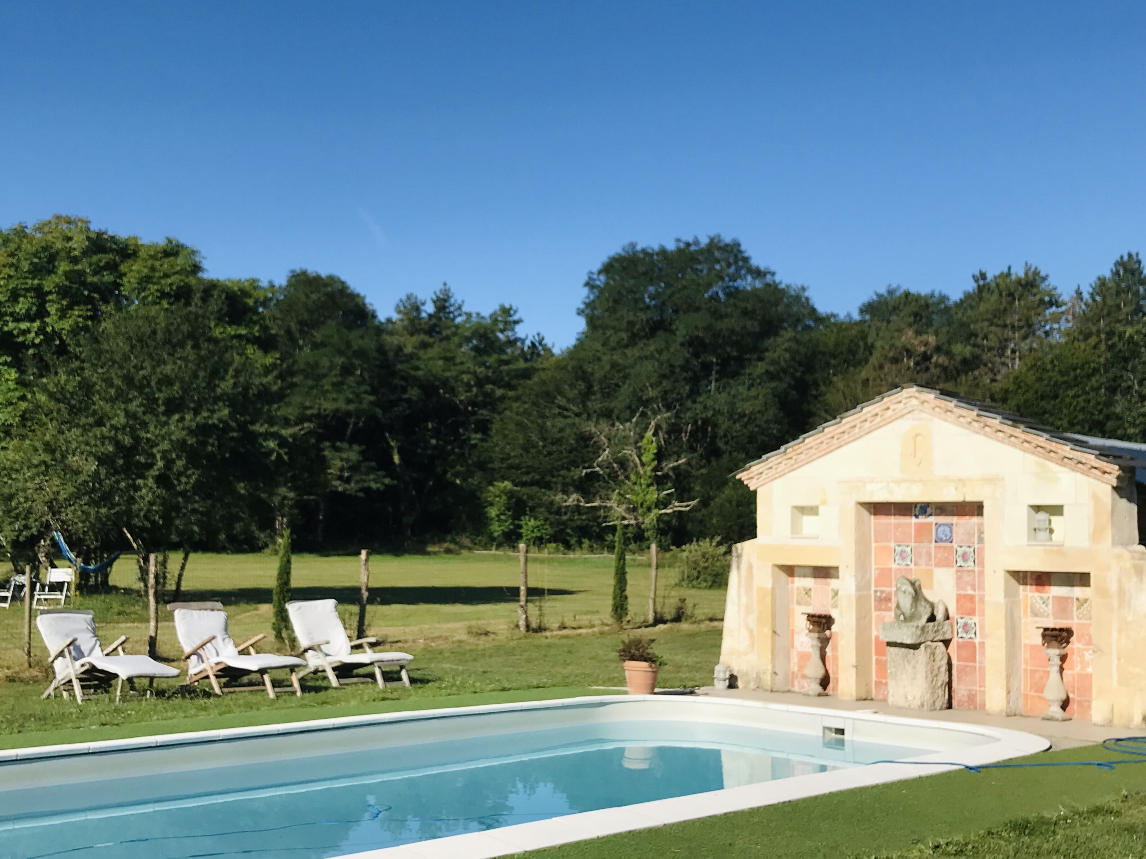 A swimming pool with lounge chairs and a small building with a tiled facade.