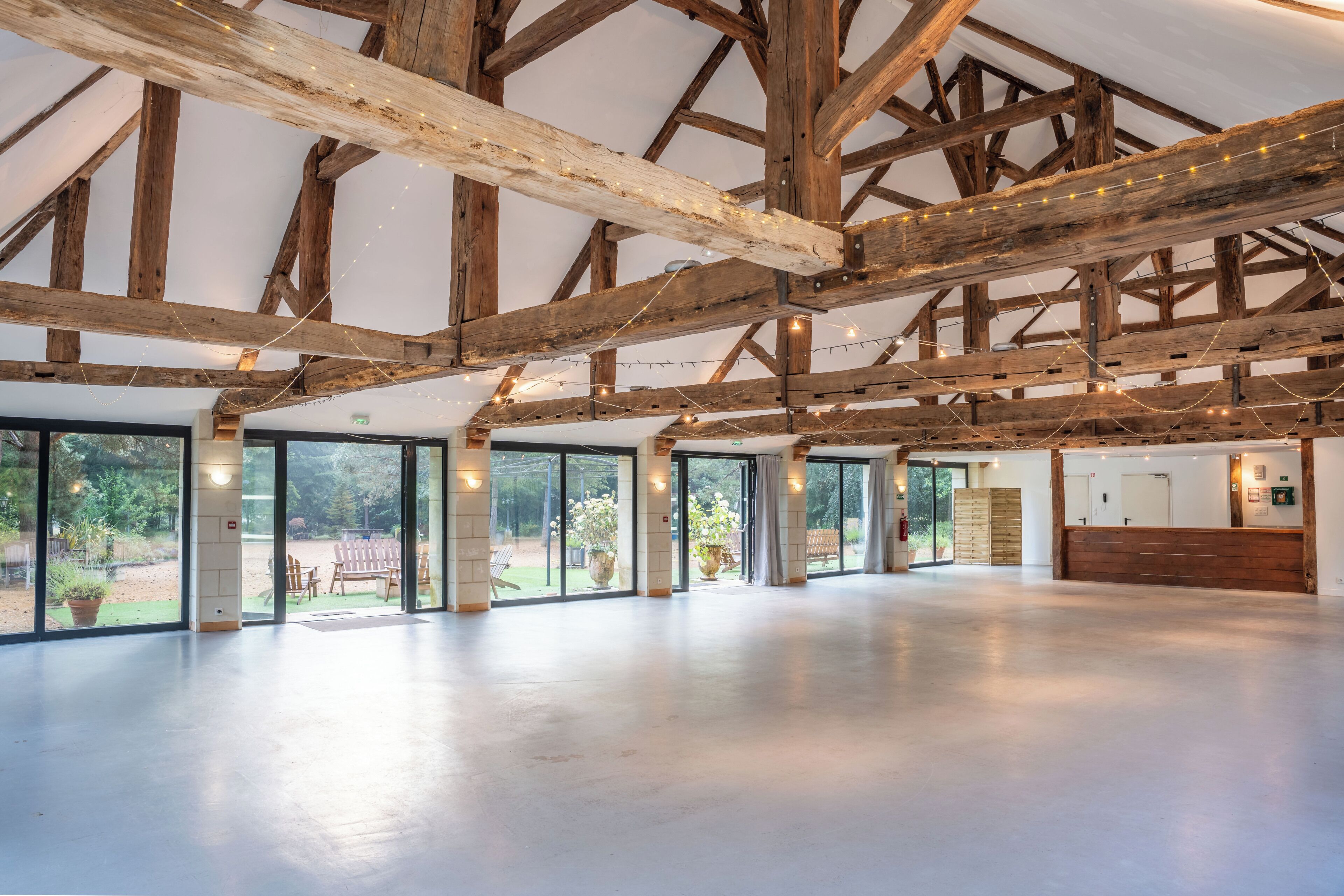 Un vaste espace intérieur doté d’un haut plafond soutenu par des poutres en bois, de grandes portes-fenêtres coulissantes donnant sur un espace extérieur, et un comptoir d’accueil.