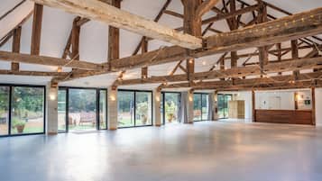 Un vaste espace intérieur doté d’un haut plafond soutenu par des poutres en bois, de grandes portes-fenêtres coulissantes donnant sur un espace extérieur, et un comptoir d’accueil.