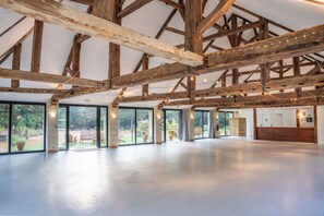 A spacious indoor area with a high ceiling supported by wooden beams, large sliding glass doors leading to an outdoor area, and a reception desk. - Château de Chambiers (Durtal)