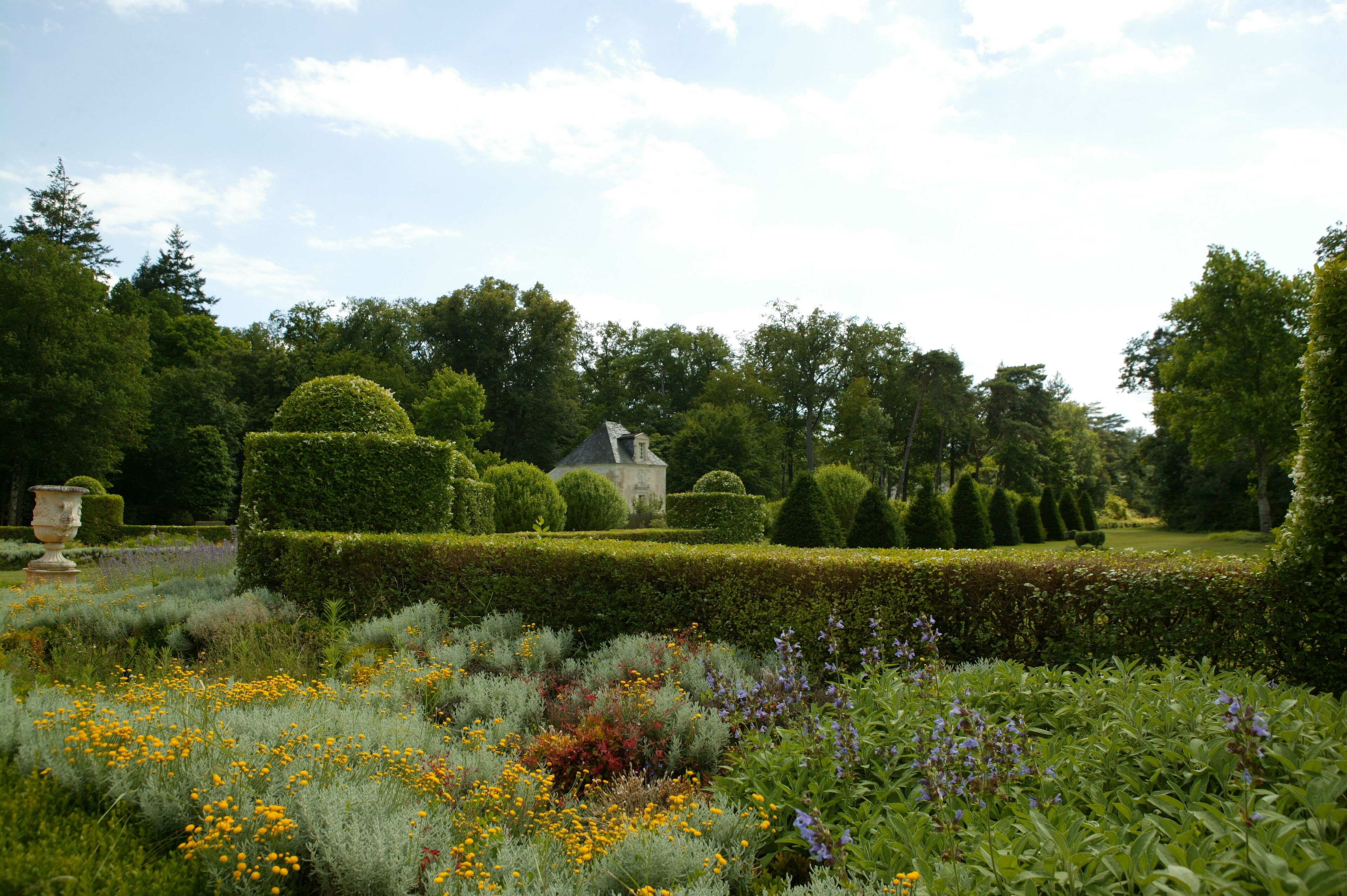 Ein gepflegter Garten mit ordentlich geschnittenen Hecken, verschiedenen Blumen und einem Gebäude im Hintergrund.