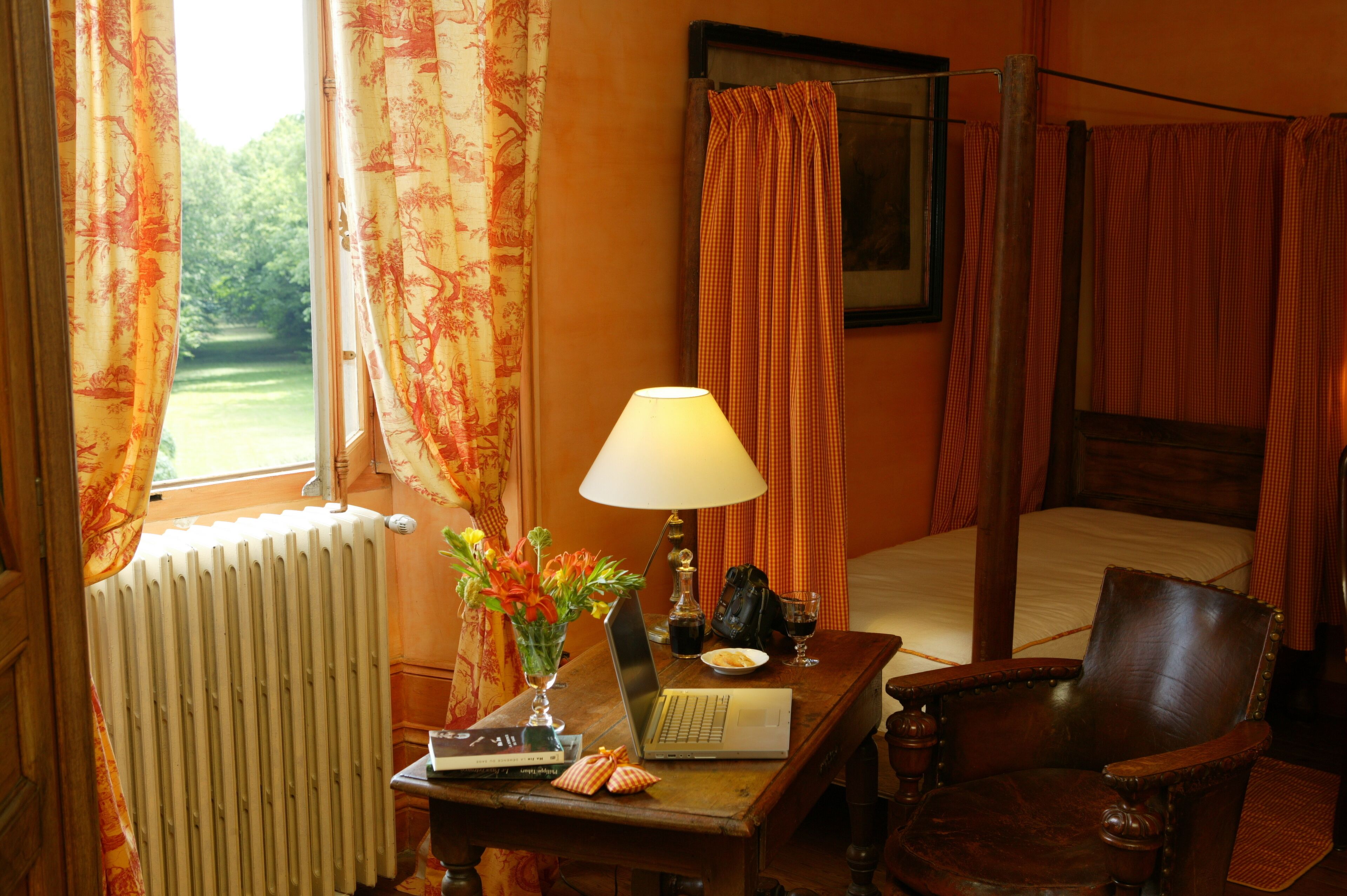Une chambre d’hôtel avec un lit, un bureau doté d’une lampe, une chaise, un radiateur et des rideaux.
