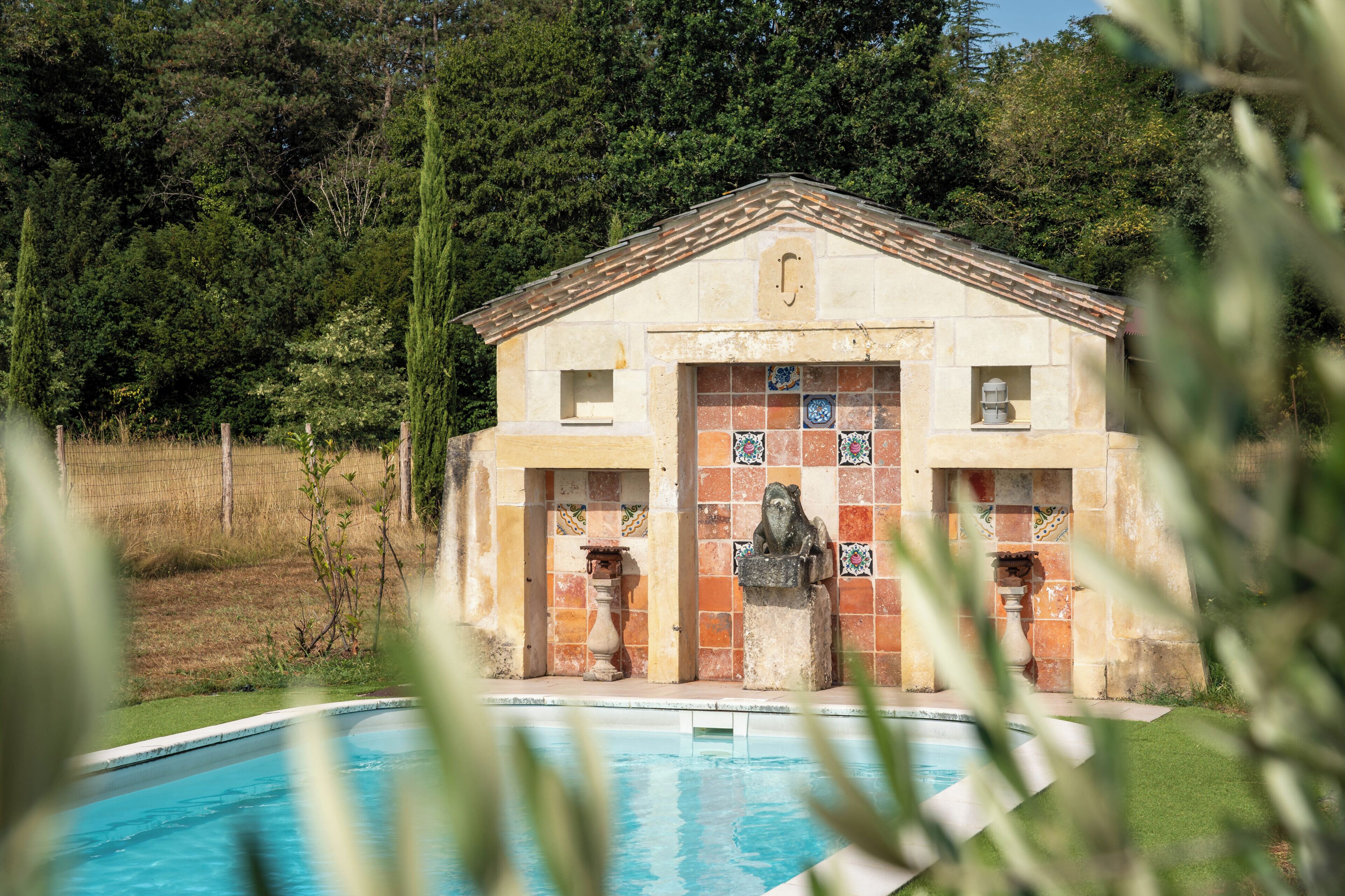 Un edificio con fachada de tejas, una piscina al frente y un paisaje natural al fondo.