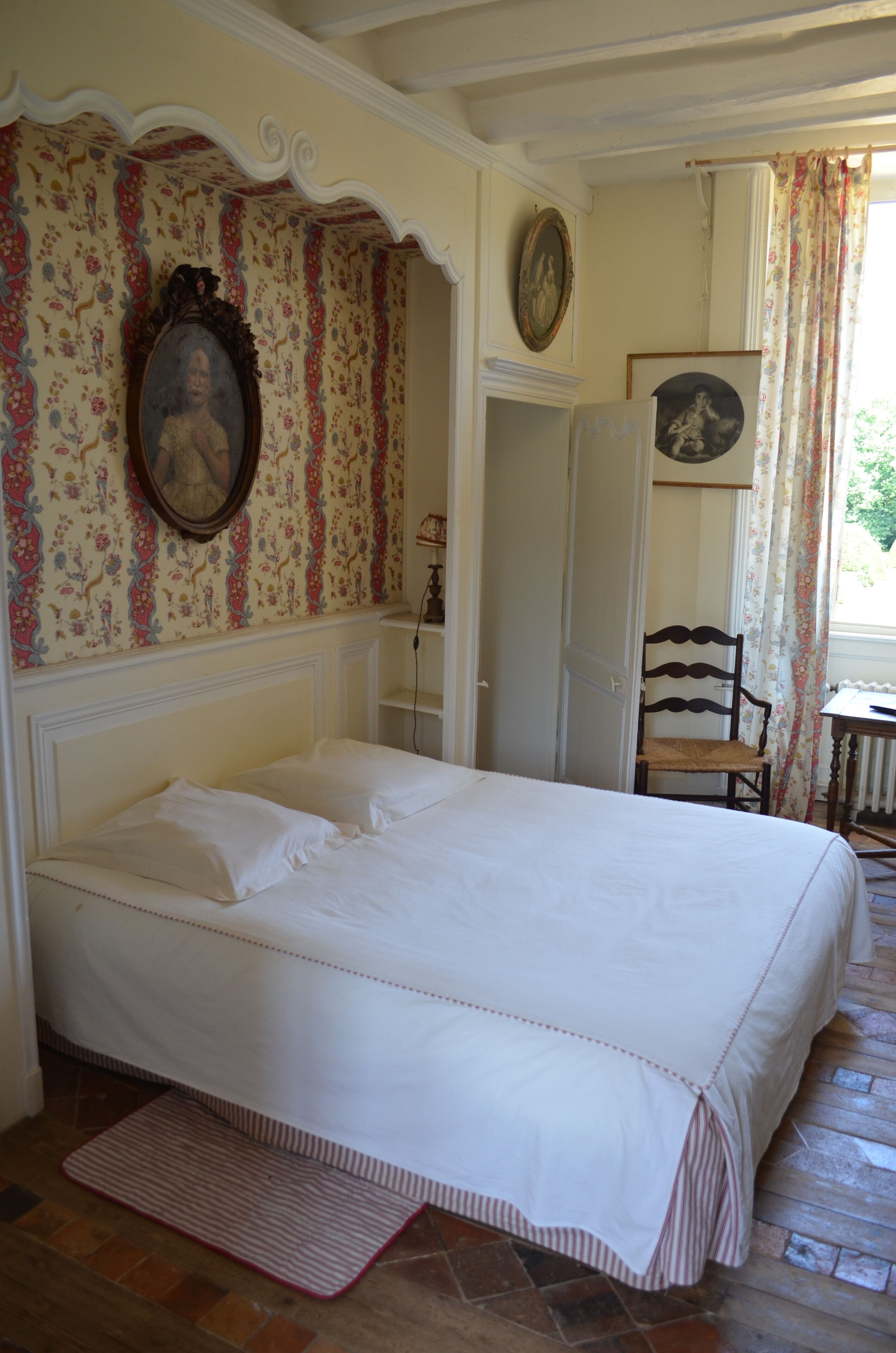 A bedroom with a large bed, a chair, a dresser, and a door leading to another room.