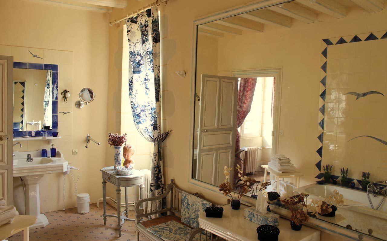 Een badkamer met een grote spiegel, een wastafel, een douche met een bloemen gordijn en een bankje.