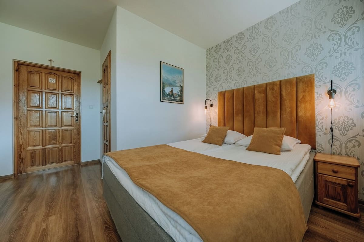 A bedroom with a large bed, wooden headboard, and a nightstand with a lamp.