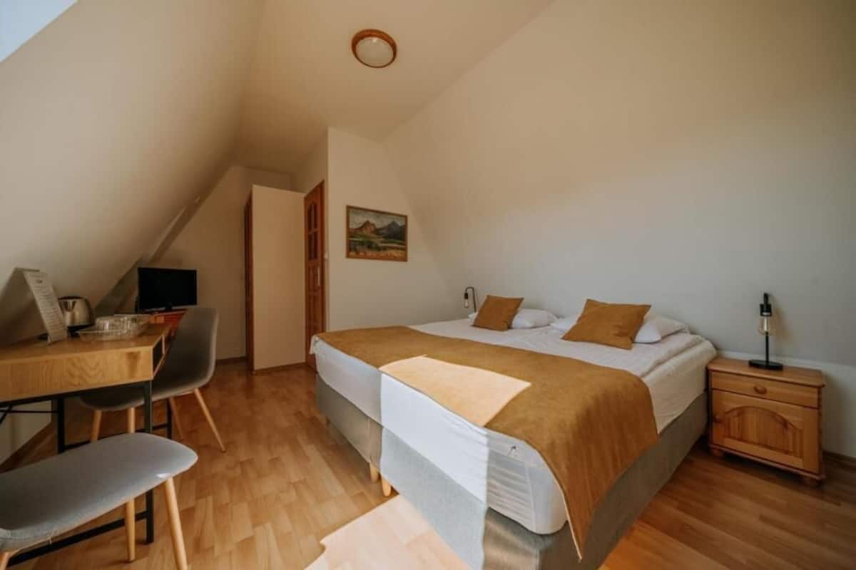 A bedroom with a bed, a desk with a chair, a nightstand, and a painting on the wall.