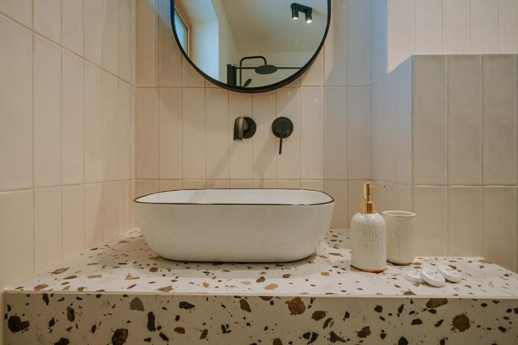 A bathroom with a white sink, a round mirror, and a speckled countertop.