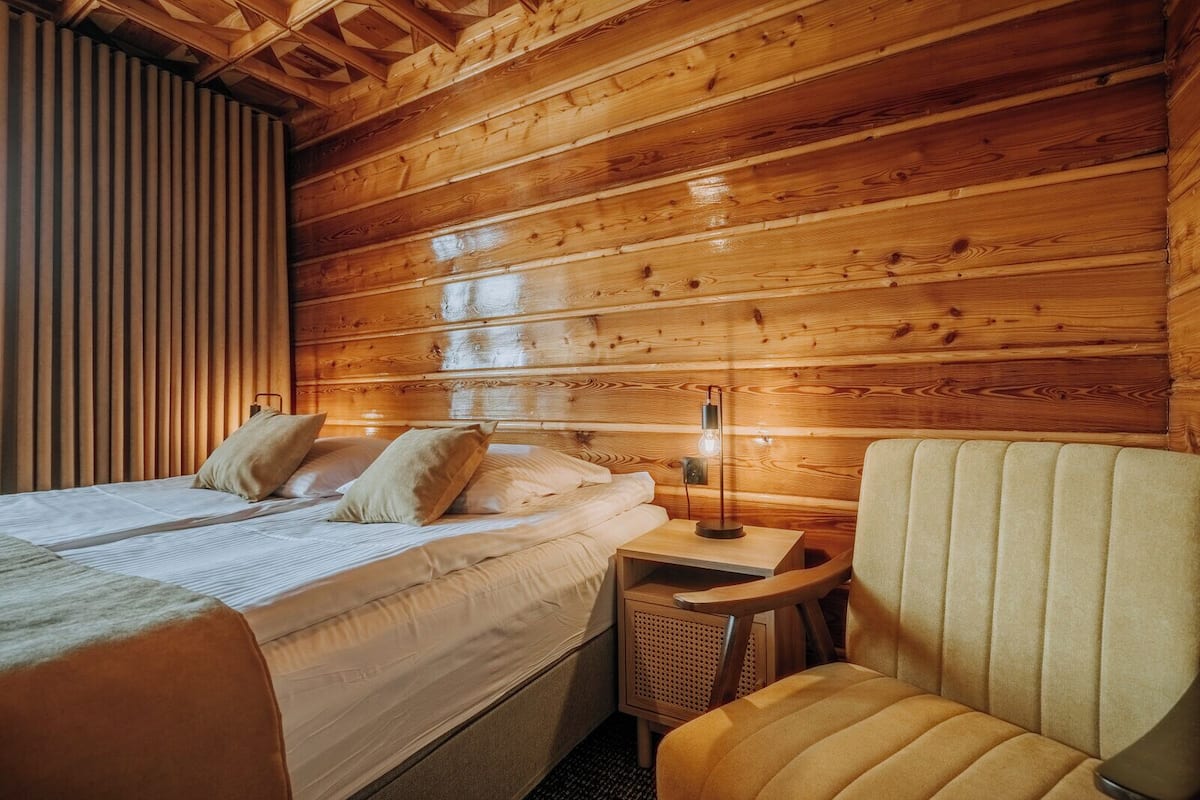 A wooden cabin room with a bed, bedside table, lamp, and a chair.