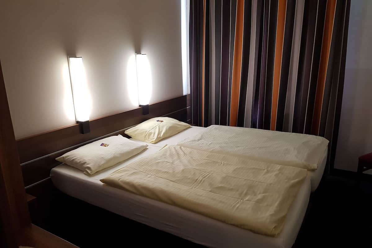 A hotel room with a bed, two bedside lamps, and a striped curtain.