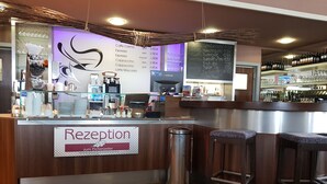Uma área de recepção com balcão de madeira, uma placa com a inscrição 'Rezeption zum Eichenzeller' e um quadro de menu acima.