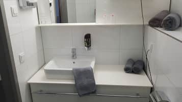A modern bathroom with a white sink, a towel rack, a hairdryer on a shelf, and a mirror.