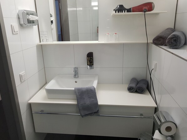 A modern bathroom with a white sink, a towel rack, a hairdryer on a shelf, and a mirror.