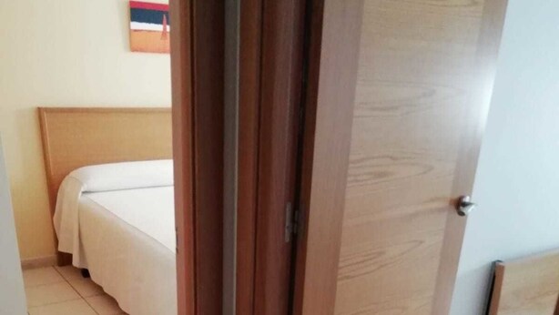 A hotel room with a bed, a wooden door, and a tiled floor. - Pensión Residencia Caola (Arteixo)