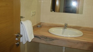 A bathroom with a wooden door, a white sink, a mirror, and a towel hanging on the door. - Pensión Residencia Caola (Arteixo)