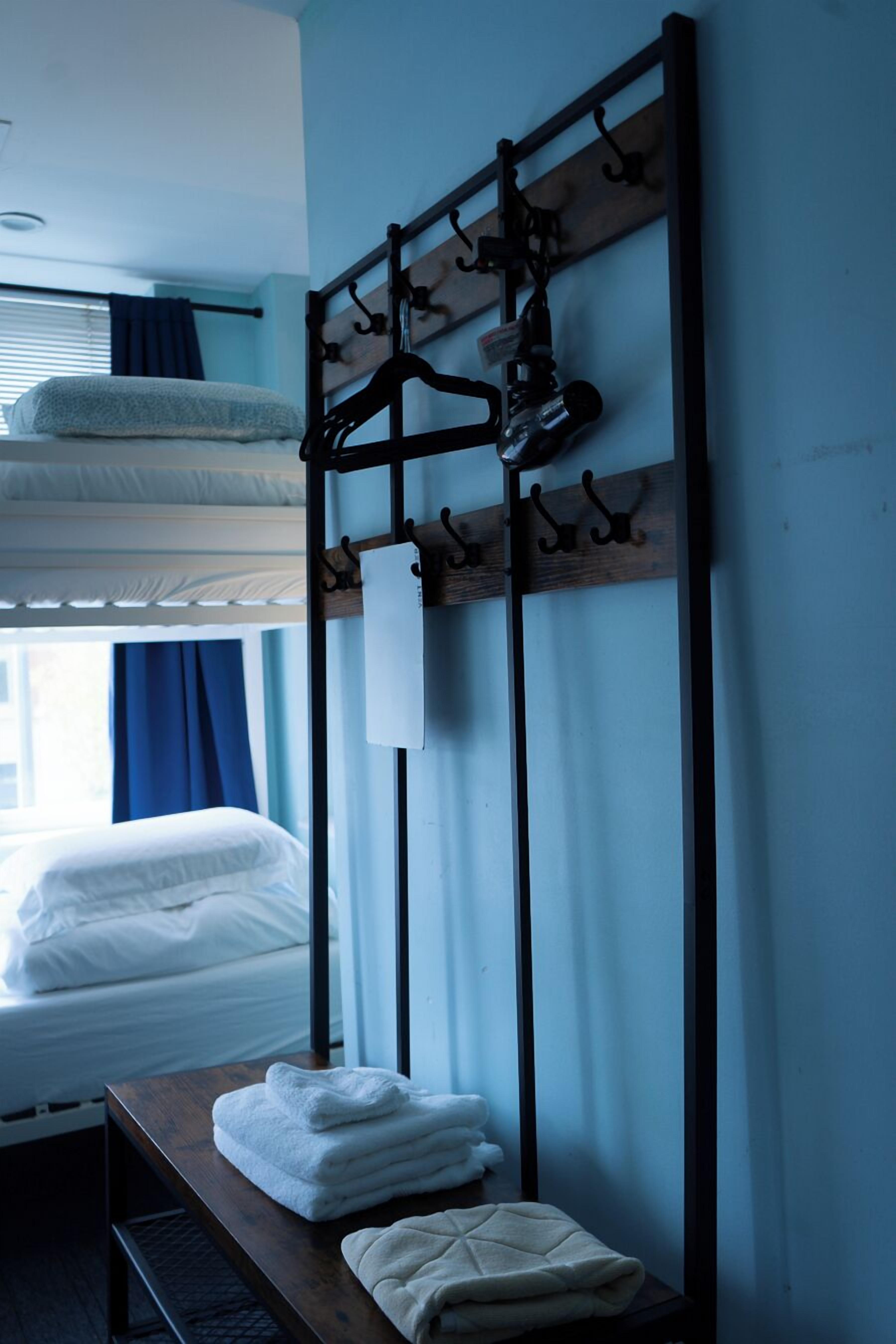 Quarto de hotel com beliches, um banco de madeira com toalhas e um porta-roupas com cabides.