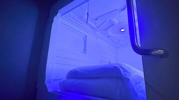 A room with a bed, a window, and a control panel with a blue light.