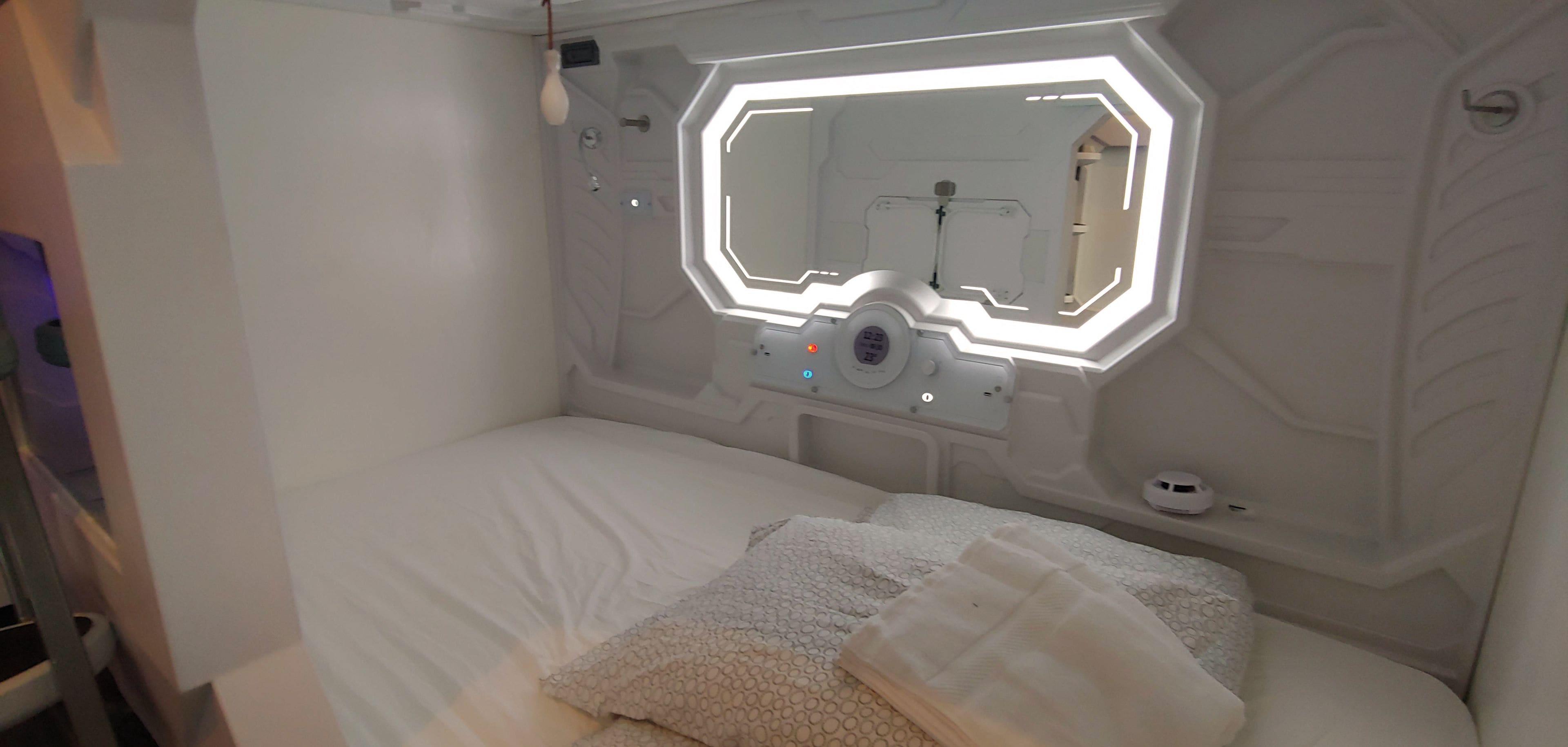 Un dormitorio moderno y minimalista con pared de diseño geométrico, cama con ropa de cama blanca y una lámpara de techo de diseño original.