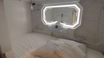 Un dormitorio moderno y minimalista con pared de diseño geométrico, cama con ropa de cama blanca y una lámpara de techo de diseño original.