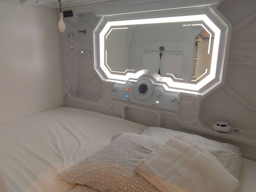 Un dormitorio moderno y minimalista con pared de diseño geométrico, cama con ropa de cama blanca y una lámpara de techo de diseño original.