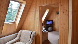A cozy attic bedroom with a sloped ceiling, a large window, a television, and a comfortable chair. - Zelenaj Dacha (Drahobrat)