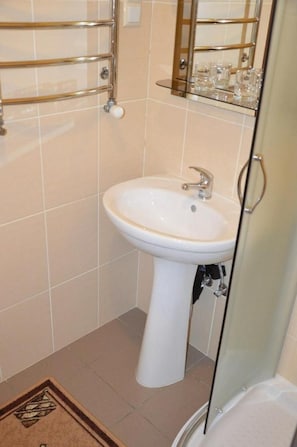 Une salle de bain avec un lavabo sur colonne, une cabine de douche en verre et un porte-serviettes avec des supports à verres.