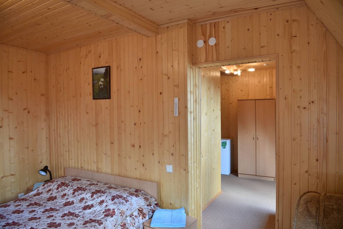Ett rum med träpanel, en säng, ett nattduksbord, en lampa, en inramad tavla och en dörr som leder till ett annat rum.