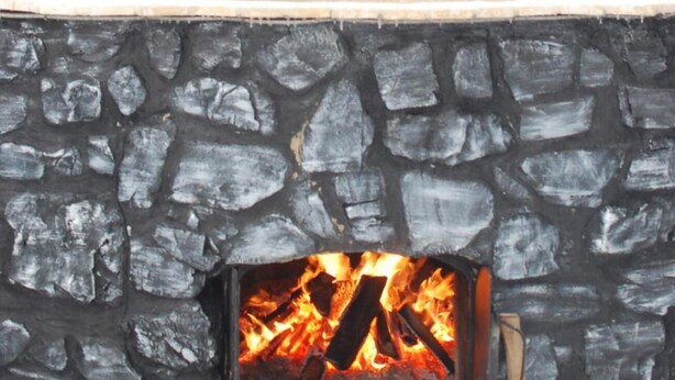 A stone fireplace with a visible fire, surrounded by a snowy forest. - Zelenaj Dacha (Drahobrat)
