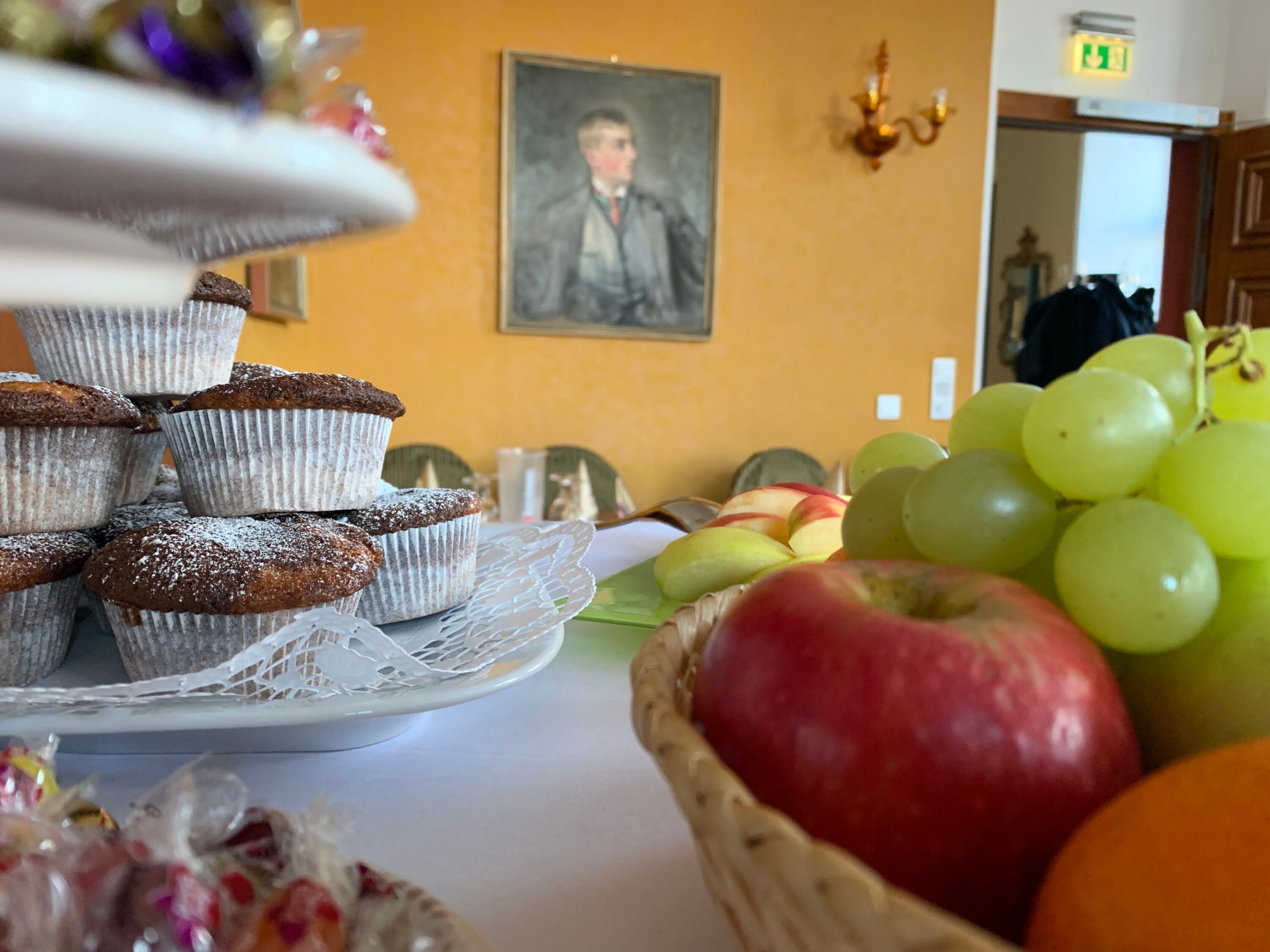 Una mesa con muffins, un plato de manzanas y una cesta de uvas.