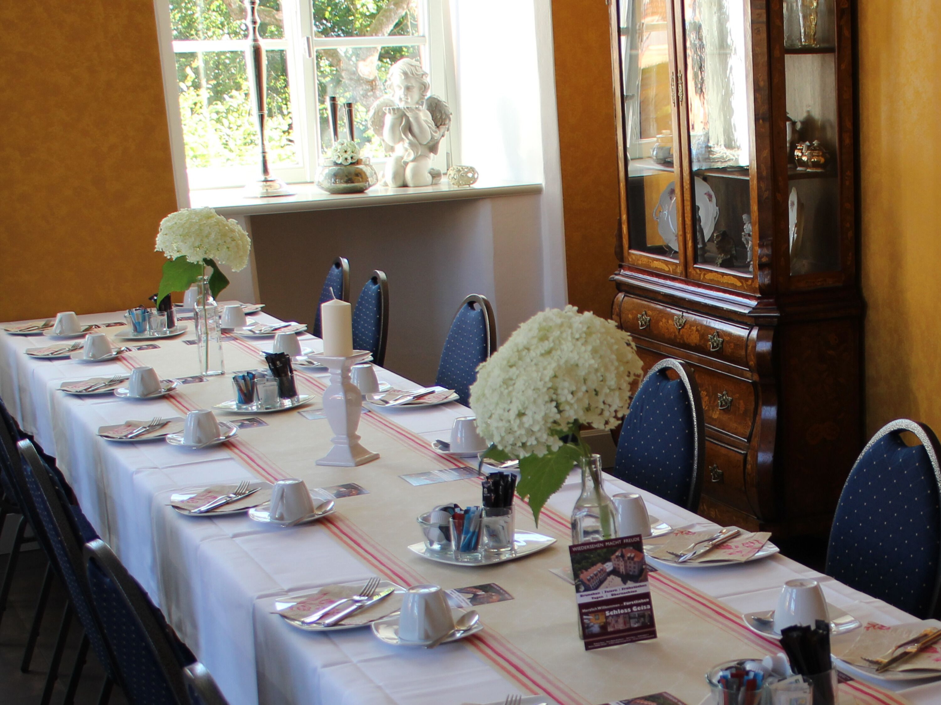Una mesa de comedor dispuesta con manteles blancos, sillas azules y flores blancas.