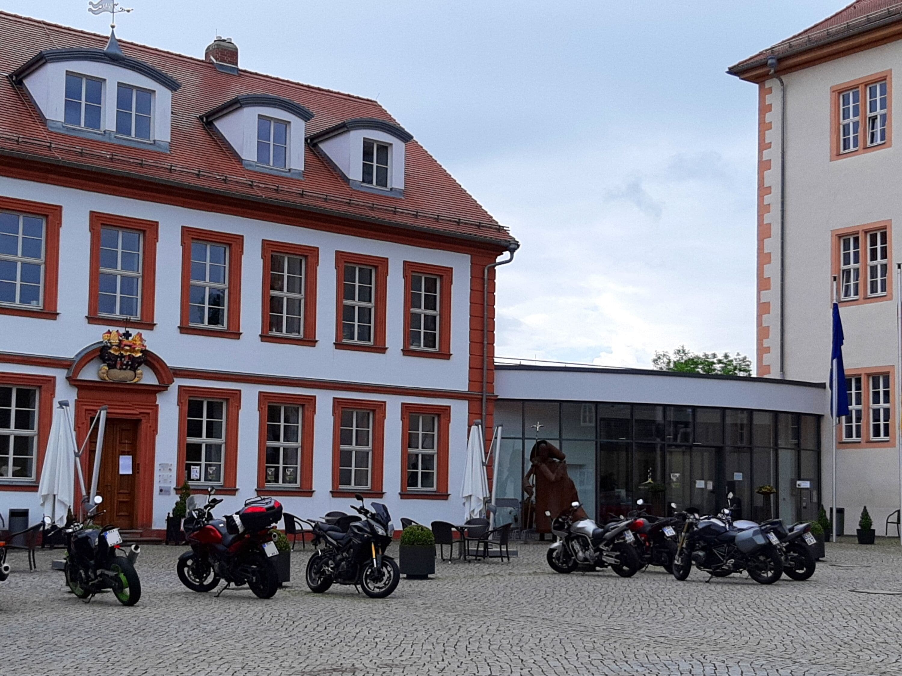A building with a red-tiled roof, multiple windows, and a coat of arms on the facade.