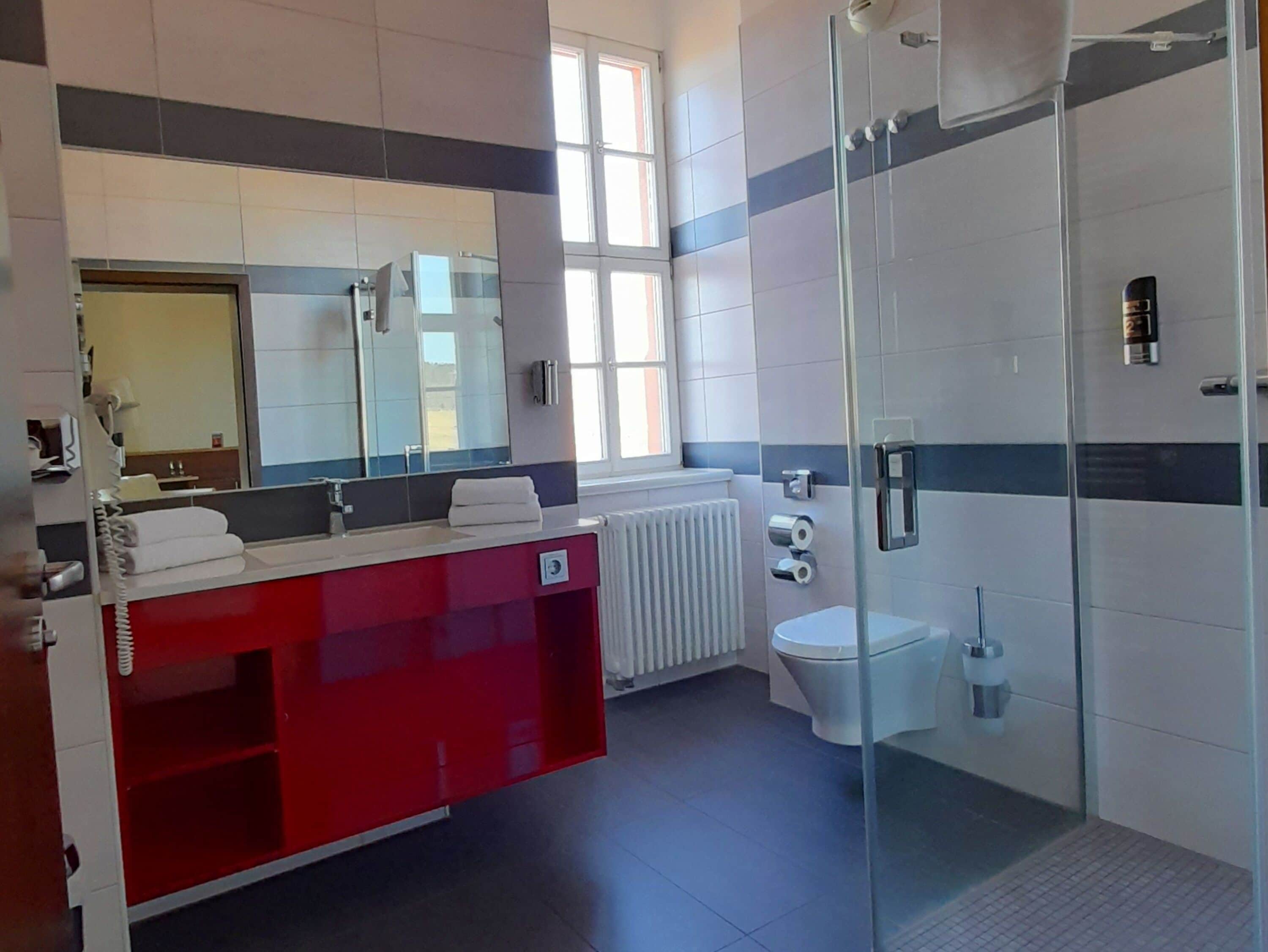 A modern bathroom with a red vanity, a glass shower enclosure, and a toilet.