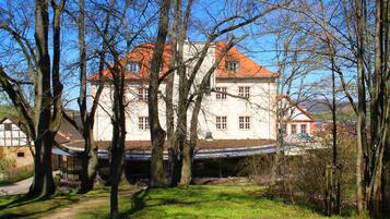 A large, multi-story building with a red roof, surrounded by trees and a grassy area.