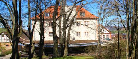 A large, multi-story building with a red roof, surrounded by trees and a grassy area.