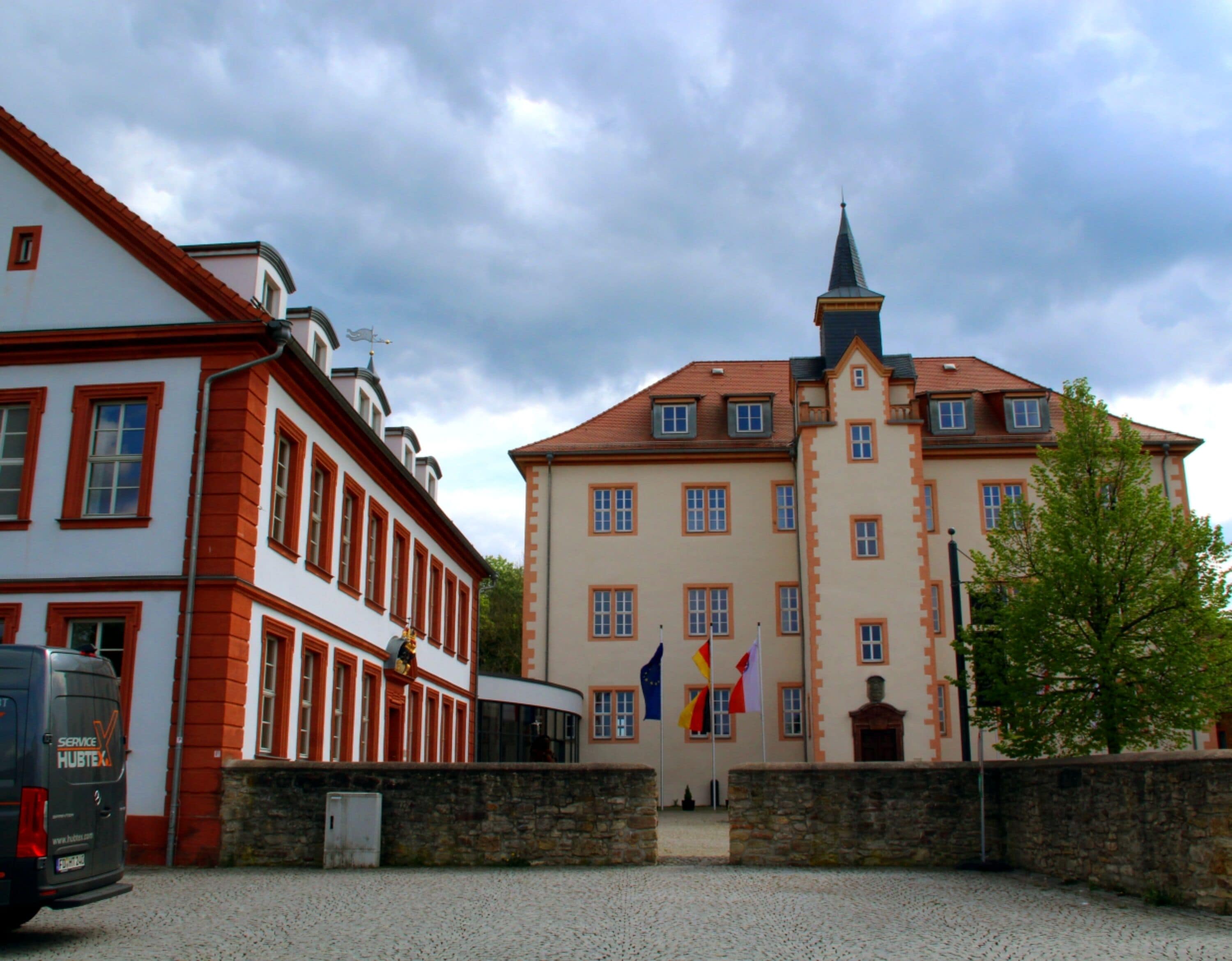 A historic building with a prominent tower and multiple flags, including the European Union flag, indicating a location of significance.